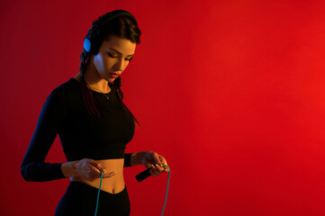 Slender beautiful sporty woman with a skipping rope listening to music in headphones