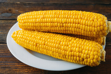 Several boiled heads of corn on a white plate on a wooden table made of boards. View from above. Delicious corn rich in vitamins