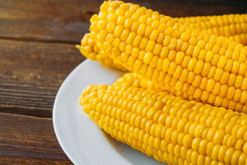 Several boiled heads of corn on a white plate on a wooden table. Close-up. View from above. Copy space.