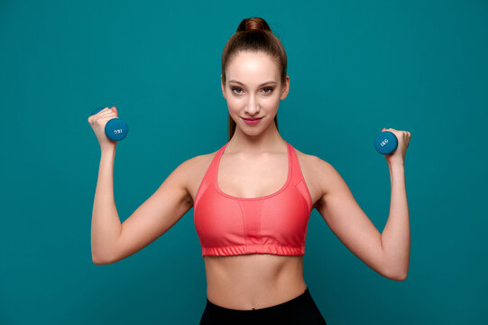 Athletic woman wearing fitness clothes exercising with dumbbell indoor