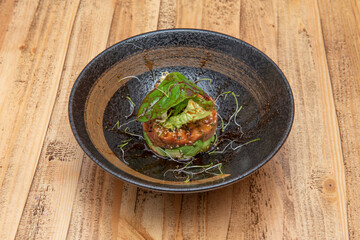 Super spicy red tuna tartare on chopped avocado, assorted lettuce sprouts leaves, bean sprouts inside a beautiful black bowl and unvarnished wooden table