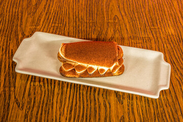 Delicious tiramisu dessert with cocoa powder and vanilla on reddish wooden table.