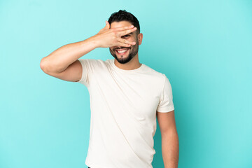 Fototapeta na wymiar Young arab man isolated on blue background covering eyes by hands and smiling
