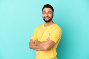 Young arab man isolated on blue background with arms crossed and looking forward
