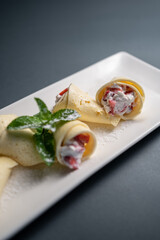 thin pancake rolls with cottage cream cheese and strawberry on black background