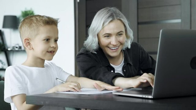 Young mother doing homework with her son pointing to something written in his notebook as he stares thoughtfully at the page