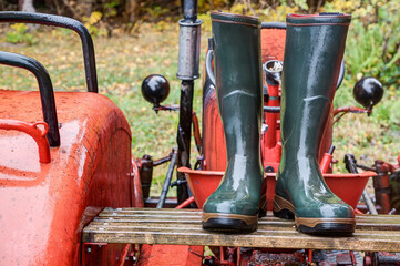 Green rubber boots stand on a bright red tractor in the rain. Wellington boots offer optimal protection on rainy days and are one hundred percent waterproof.