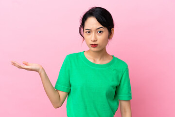 Young Vietnamese woman isolated on pink background having doubts