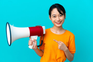 Young Vietnamese woman isolated on blue background holding a megaphone and pointing side