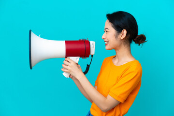 Young Vietnamese woman isolated on blue background shouting through a megaphone to announce something