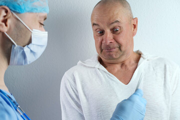 Obraz premium young male doctor in a blue uniform jokes with an old male patient, senior looks at the instrument with apprehension, treatment of people