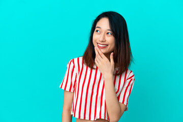 Young Vietnamese woman isolated on blue background looking up while smiling