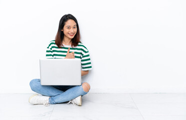 Young Vietnamese woman with a laptop sitting on the floor isolated on white wall giving a thumbs up gesture