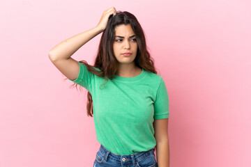 Young caucasian woman isolated on pink background having doubts while scratching head