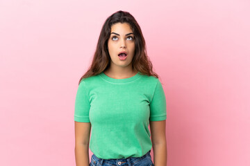 Young caucasian woman isolated on pink background looking up and with surprised expression
