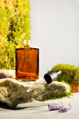 Amber cosmetic bottle with dropper on a natural stone podium. Natural stone, bricks with moss in a background on a light background. Perfect for a natural cosmetic brand serum or oil.
