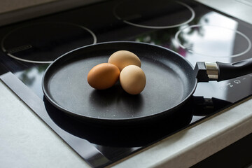 three raw eggs are lying in a frying pan in the kitchen