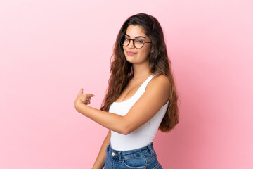 Young caucasian woman isolated on pink background pointing back