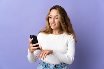 Fototapeta premium Young blonde woman isolated on purple background sending a message or email with the mobile