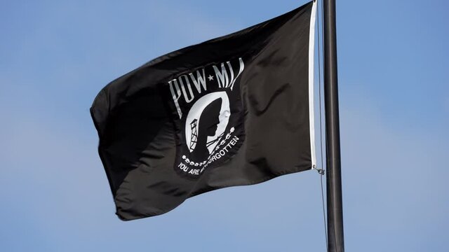 This slow motion video shows a POW MIA flag flying in the wind against a clear blue sky.