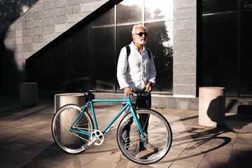 Man in White shirt poses with bicycle. Attractive white haired guy in light fashionable outfit and...