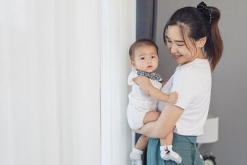 mother holding newborn baby in a tender embrace near window in bedroom