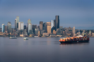 A container ship freighter sits at anchor in Elliott Bay on Puget Sound as the Seattle Skyline rises in the background. - obrazy, fototapety, plakaty