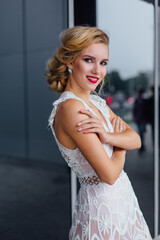 Fototapeta premium Beautiful blond bride in white wedding dress standing near mirror window outdoors.