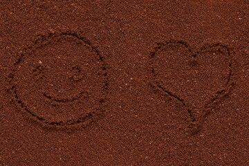 Drawing of a smiling face and heart on the surface of crushed coffee. Coffee texture. 