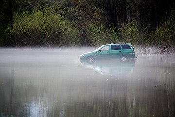 a green car drowned in water is standing in the middle of the forest in the fog