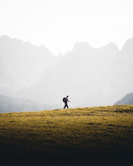 Lone male hiker walking on a grassy hill against a misty mountain landscape