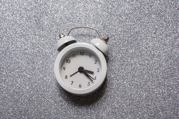 Closeup of a white alarm clock on a gray glitter background