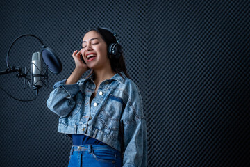 Happy cheerful pretty smiling of portrait of young Asian woman vocalist Wearing Headphones recording a song front of microphone in a professional studio