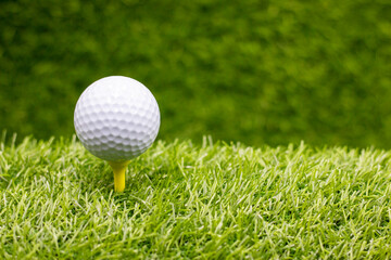 Golf ball is on yellow tee ready to tee off on green grass