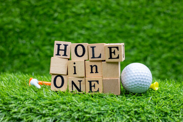 Hole in one wooden black with golf ball are on green grass with tee. n golf, a hole in one or hole-in-one (also known as an ace, mostly in American English) occurs when a ball hit from a tee to start  - obrazy, fototapety, plakaty