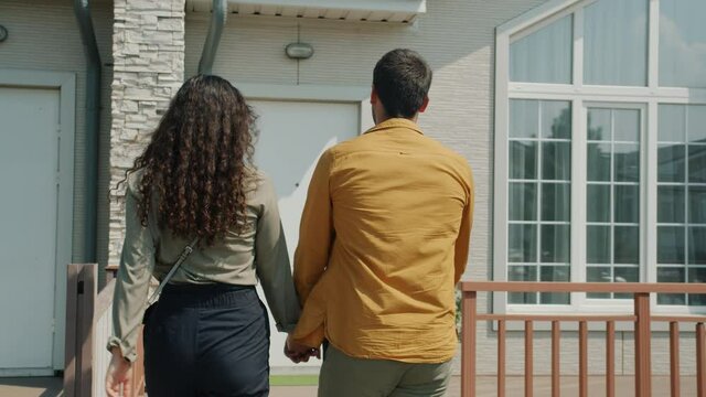 Joyful husband and wife walking to new house front door talking smiling outdoors in beautiful sururban street. Relationship and property concept.