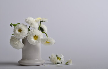 A bouquet of white daisies in a white ceramic pile.