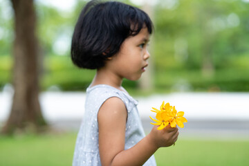 Little Asian girl holding yellow flowers at field.