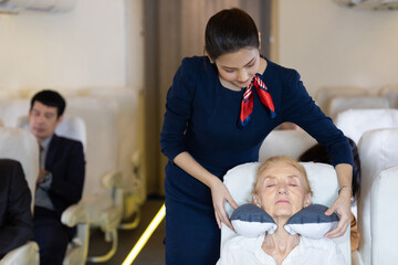 flight attendant or air hostess giving a pillow to senior woman when sleeping during a flight