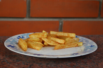 Closeup of  ceramic plate of fried potatoes on the table with brick wall on the background