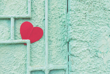 Red paper heart on a rustic green crumbling wall.the heart is pinned to an iron rod