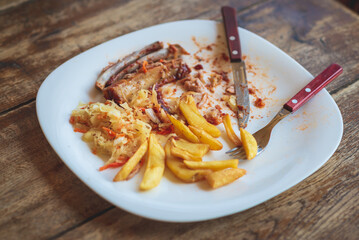 Leftover food on place after partying.Closeup fork,knife on the plate blank after food on the table.