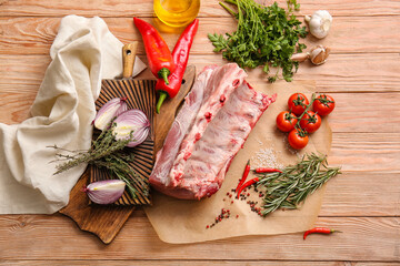 Parchment with raw pork ribs, spices and vegetables on wooden background
