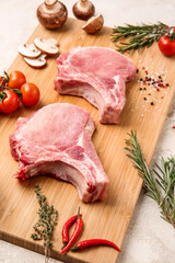 Board with slices of raw pork meat, spices and vegetables on light background