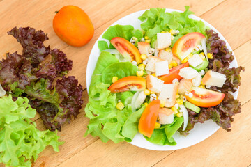 Mixed fresh vegetables salad in white dish on wood plate
