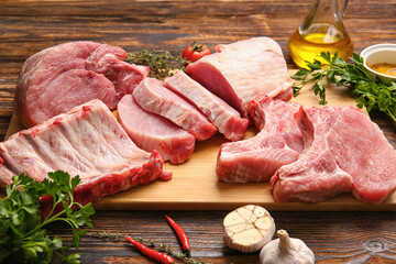 Board with slices of raw pork meat, parsley and garlic on wooden background