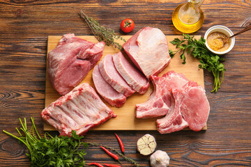 Board with slices of raw pork meat, spices and vegetables on wooden background