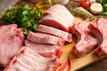 Board with slices of raw pork meat, parsley and chili pepper on wooden background, closeup