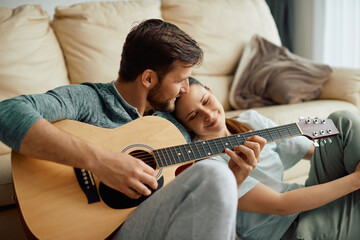 Romantic man plays acoustic guitar for his wife at home.