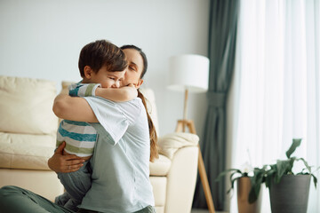 Obraz premium Loving mother hugs and kisses her small son at home.